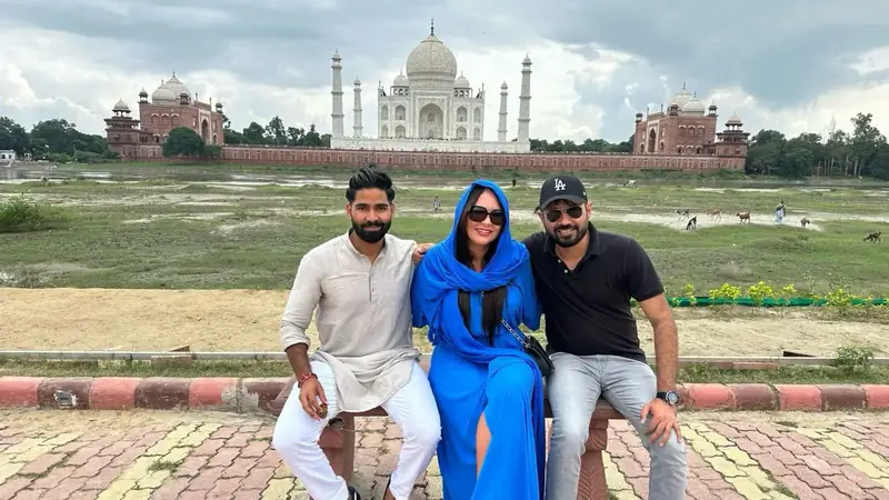 Tres personas sentadas en un banco con el Taj Mahal al fondo, desde la orilla opuesta del río Yamuna, en Agra
