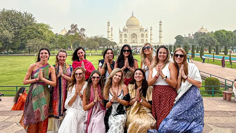 Grupo de viajeras latinoamericanas saludando con las manos juntas frente al Taj Mahal en Agra