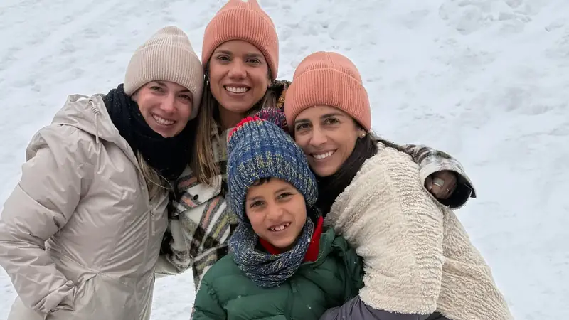 Un niño con gorro de lana y bufanda sostiene una bola de nieve mientras tres mujeres lo abrazan, sobre la nieve del puerto de Khardung La, en Ladakh, India.