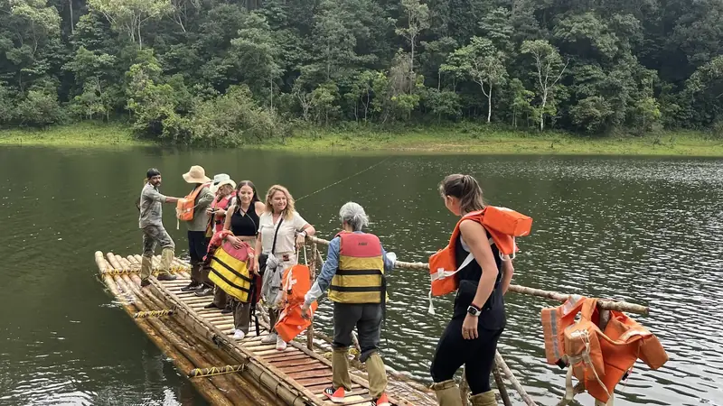 Viajeros en una balsa de bambu sobre un lago rodeado de selva en los Ghats occidentales, sur de la India