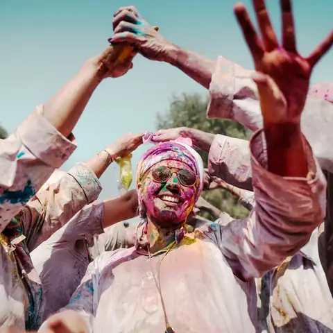 Hombre sonriente lanzando polvo de color al aire durante el festival Holi en la India