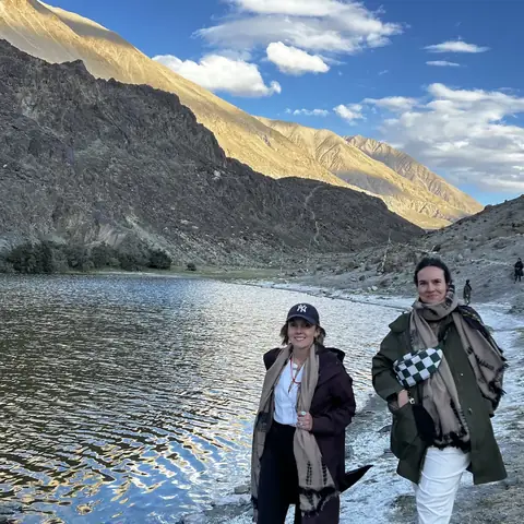 Dos viajeras a la orilla de un lago de montaña bajo picos áridos en Ladakh