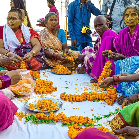 Grupo de mujeres indias tejiendo guirnaldas de flores de caléndula sentadas junto al río