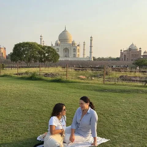 Pareja de viajeras sentadas sobre el césped con el Taj Mahal al fondo al atardecer, Agra
