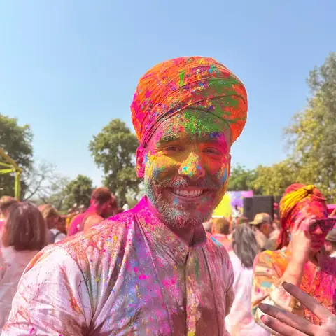 Hombre con turbante naranja y el rostro cubierto de polvo rosa sonríe durante el festival Holi