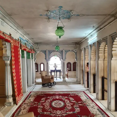 Galería de mármol con arcos, lámpara verde y alfombra roja en el City Palace de Udaipur