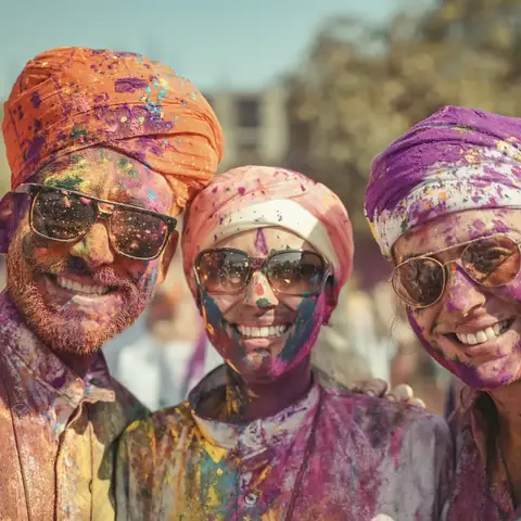Tres hombres con turbantes y la cara cubierta de polvo rosa y naranja sonríen durante el festival Holi