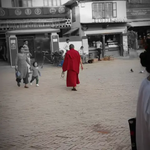 Monje con túnica granate cruza una plaza de Katmandú, fotografía en blanco y negro con un toque de color