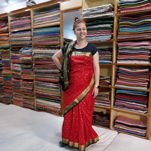 Viajera con un sari rojo posando ante estanterías llenas de telas de colores en una tienda tradicional