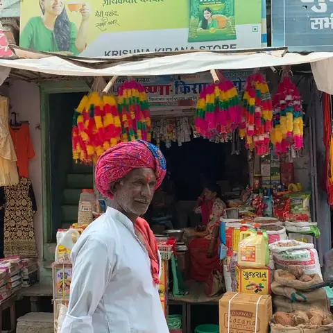 Hombre con turbante de pie en la entrada de su tienda de artesanías y guirnaldas