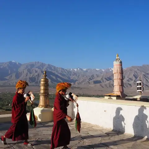 Dos monjes budistas con caracolas caminan por la azotea del monasterio de Thiksey, con el valle del Indo detrás
